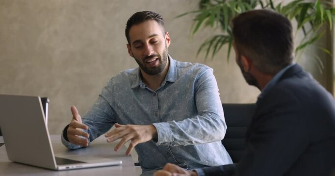 Sales manager consulting client in office, sit at desk make speech, explain contract details, selling company services. Two male colleagues brainstorming, discussing ideas and thoughts at workplace