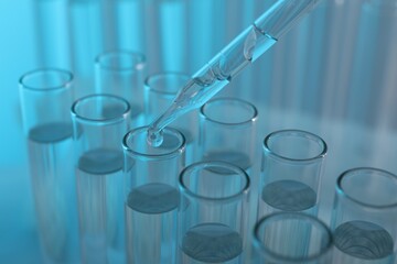 Laboratory analysis. Dripping liquid from pipette into glass test tube on light blue background, closeup
