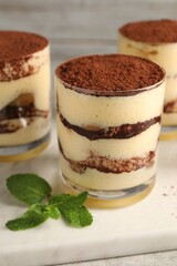 Delicious tiramisu in glasses and mint on table, closeup