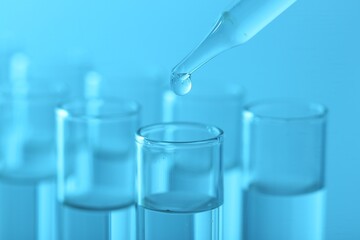 Laboratory analysis. Dripping liquid from pipette into glass test tube on light blue background, closeup