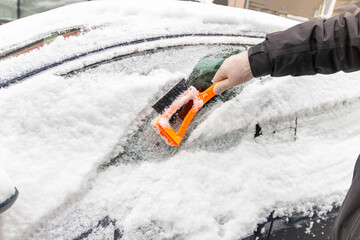 Winter season driving. Close-up of a hand cleaning a vehicle's windshield from ice and snow. Transportation, winter, weather, people and vehicle concept