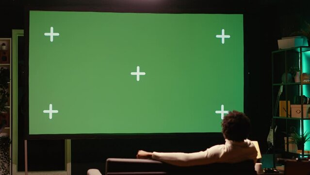 African american man watching football competition live on widescreen chroma key smart TV, cheering for favorite team. Sports fan on couch in front of green screen television set celebrating goal