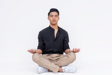 A young southeast asian man sitting indian style, trying to meditate and relax. Studio shot...