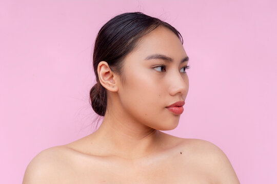 Portrait of a poised Asian woman looking 45 degrees, with a graceful pose against a soft pastel pink backdrop, exuding confidence and tranquility.