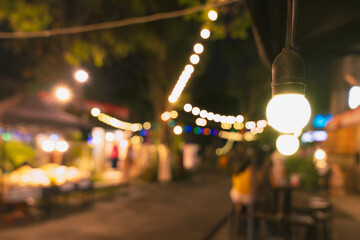 Decorative outdoor string lights hanging on electricity post in the garden at night time with blur...