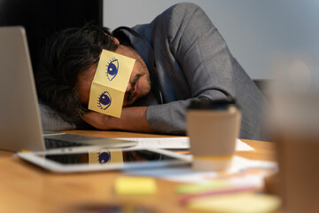 Cheerful adult man resting in office with sticky notes on the eyes. Sleeping man having stickers...