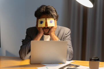 Sleeping clerk hides eyes with sticky notes, open eyes drawn on adhesive papers, he wants to sleep...