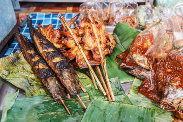 Various side dishes street food of thailand. Grilled catfish on skewers, grilled chicken on skewers and other side dishes in a tray with banana leaves on the stall.