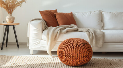 Knitted pouf near white fabric sofa with blanket and terra cotta pillows. Scandinavian, hygge style home interior design of modern living room