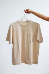 Woman holding a beige t-shirt mockup with pocket on a white clothes hanger.