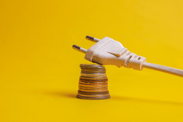 White electrical plug with stacked coins isolated on yellow background. Concept of low electricity...