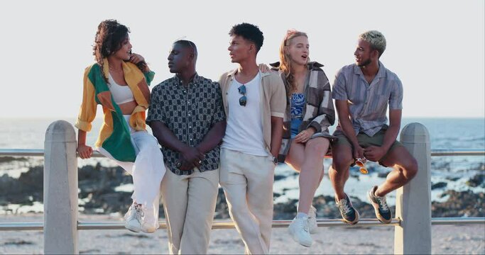 Friends, ocean and holiday in group, talking and promenade in summer, relax and gen z culture with fashion. Men, women and diversity by sea, beach and relax on railing on vacation with solidarity