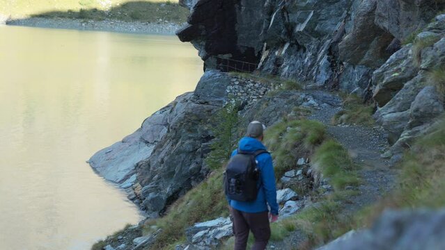Racking Focus On Rock And Tourist Hiking On Mountain Trail By The Lake In Cima Fontana, Valmalenco, Italy. handheld shot