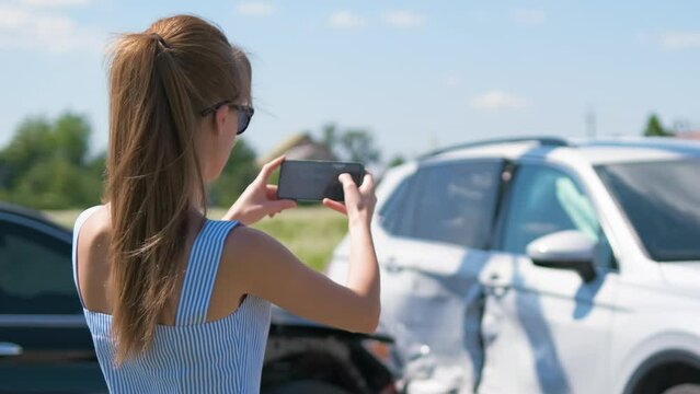 Stressed woman driver taking photo on mobile phone camera after vehicle collision on street side for emergency service after car accident. Road safety and insurance concept