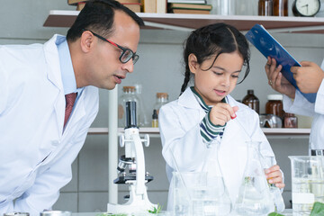 Asian scientist kid student and Indian teacher with plant at biology class in school laboratory, do an experiment, learning, teaching with microscope, test tube. Education, science and school concept