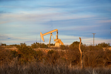 Solo pumpjack on the edge of West Texas lake bathed in late afternoon sunlight.