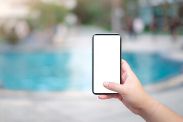 Woman hand showing white empty smartphone screen on hotel pool background. Mobile App...