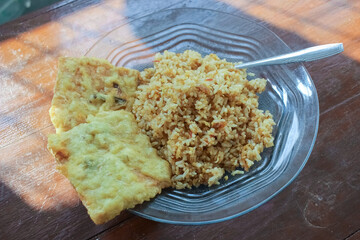photo of a breakfast dish that is on the table with a menu of egg fried rice with 2 fried tempeh and served in a glass plate