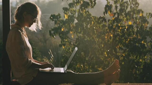 Young blonde woman using laptop while sitting on the rooftop in sunlight. Remotely working concept.