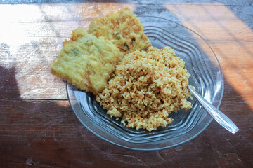 photo of a breakfast dish that is on the table with a menu of egg fried rice with 2 fried tempeh and served in a glass plate