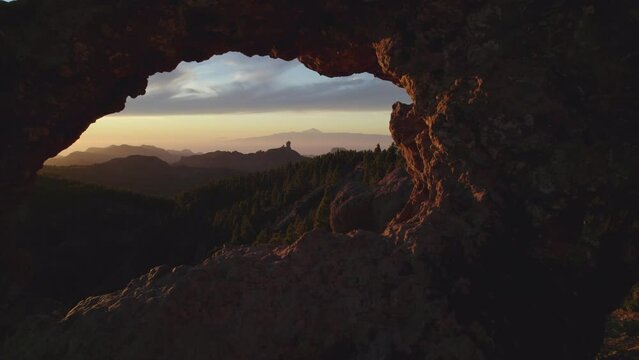 Cinematic shot going through the window of Roque Nublo in reverse during sunset. The majestic Teide volcano can be seen. Gran Canaria.