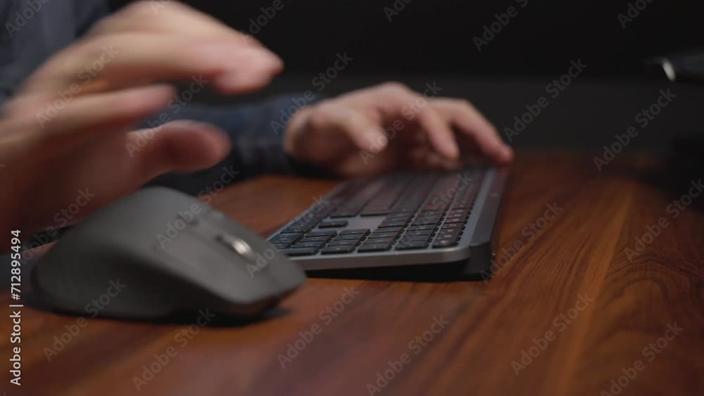 Poster person’s hands using a computer mouse and keyboard on a wooden desk.