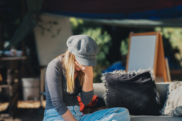Girl covering her eyes sitting on a sofa in a forest , wearing a grey hat . Stock Photo 