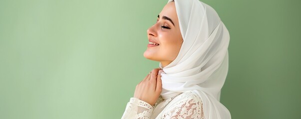 Side view portrait of young beautiful asian muslim woman wearing hijab looking away and smiling while standing against green background - obrazy, fototapety, plakaty