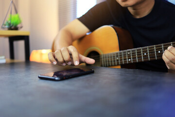 Man using smartphone to sound recording or learn acoustic guitar by video lesson