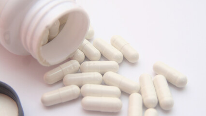 White pills spilling out of pill bottle. Focus on foreground, soft bokeh.