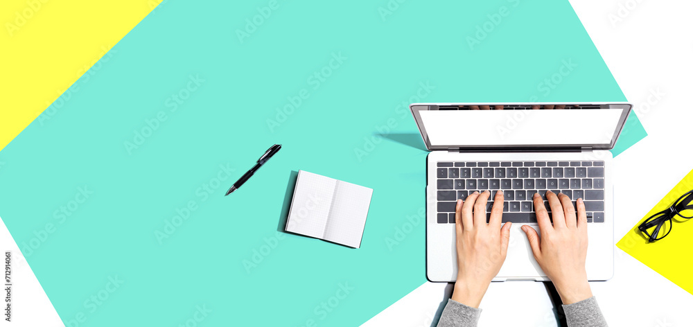 Poster person using a laptop computer with a notebook and eyeglasses - flat lay