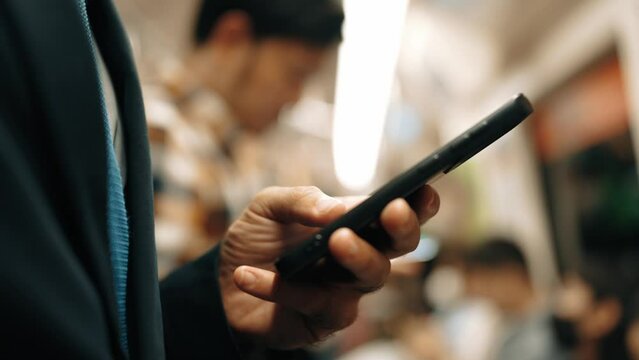 Closeup of business man hands looking phone while standing at train surrounded by people. Project manager checking email, planing marketing strategy by using phone with blurred background. Exultant.