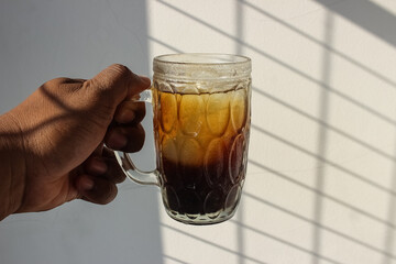 photo of an iced coffee drink in a large glass cup being held by a man against a white wall...