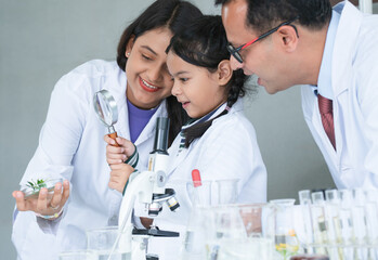Asian scientist kid student and Indian teacher have fun with plant at biology class in school laboratory, do an experiment, using magnifying glass and microscope. Education, science and school concept