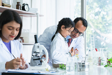 Asian scientist kid student and Indian teacher looking at plant in test bottle at biology class in...