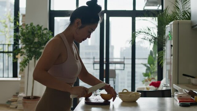 asiatic woman in slow motion cutting pear fruit in her modern kitchen apartment room with skyline cityscape of modern city view from window