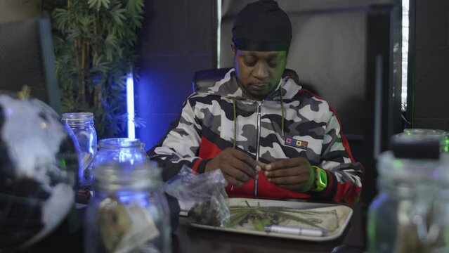 straight on view of a black man  inserting the tobacco wrapper in his mouth to seal a blunt  or marijuana cigarette closed