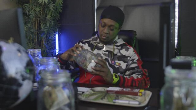 a black man inspects a mason jar filled with marijuana then opens it to smell the aroma of the pot