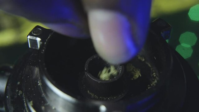 close up of a black mans hand as he slowly breaks up marijuana bud into the bowl of a vaporizer preparing to smoke the pot