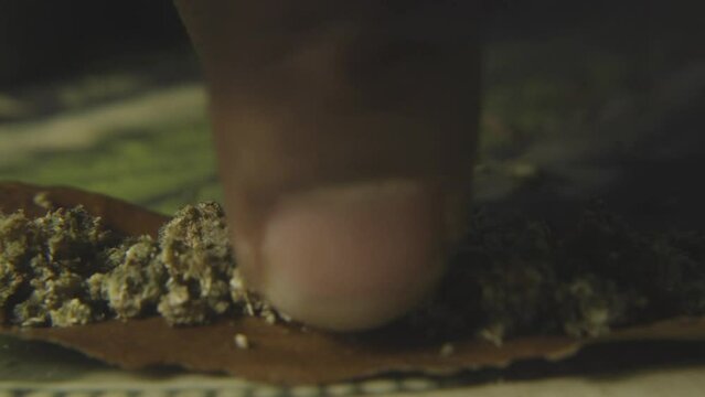close up of a black mans finger lining up the ground cannabis bud to prepare to roll a blunt of marijuana