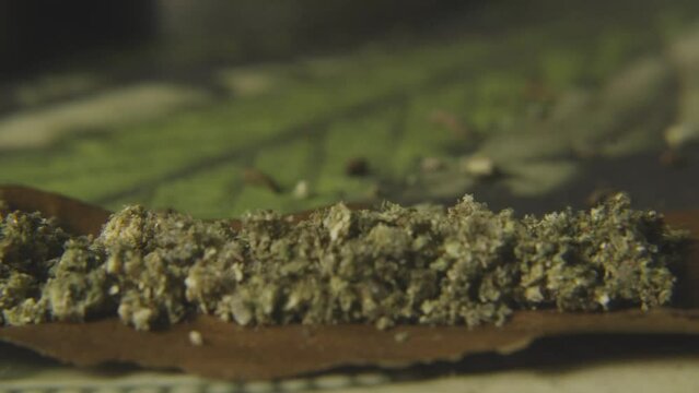 a black mans hand breaking up marijuana budss onto a hemp wrapper to prepare to roll a blunt