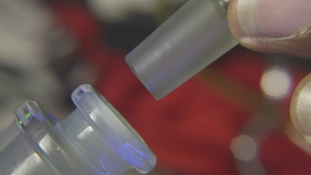 side view of a black mans hand placing the stem of a glass bowl filled with pot onto a water bong  that is used for smoking marijuana