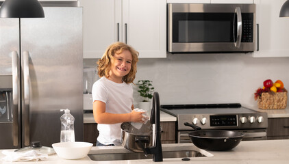 Home chores. Kid in kitchen cleaning plates. Cute boy washing dishes in domestic kitchen. Child boy washing dishes in the kitchen interior. Child helping his parents with housework.