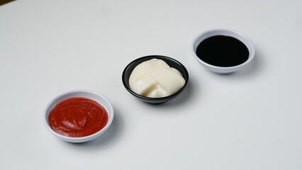 Obraz na płótnie Canvas three sauces ketchup mayonnaise, sweet soy sauce and chili sauce in black bowl isolated on white background