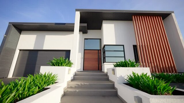 Executive style home front with large double wide wooden door entrance exterior of house. Modern architecture manicured gardens grey roller door stone steps leading up to front door.