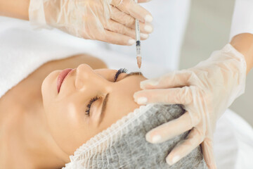 Hands of cosmetologist in gloves making rejuvenation anti wrinkle injection in beautiful woman face skin in a beauty spa salon. Cosmetic procedure, aesthetic cosmetology and facial treatment concept.