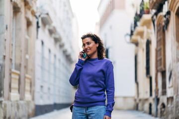 Positive woman talking on smartphone in city - 712932495