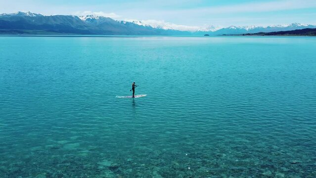 Adventurous serenity: Paddle boarder with Mount Cook backdrop in captivating stock footage. Tranquil waters meet majestic peaks.