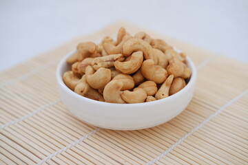 Roasted cashew nuts in white bowl on bamboo mat, stock photo