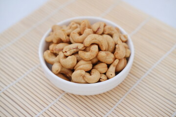 Roasted cashew nuts in white bowl on bamboo mat, stock photo